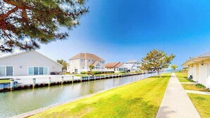 A residential area with houses along a canal, a grassy pathway, and a clear sky. - Beach Club  135 D (Ocean City)
