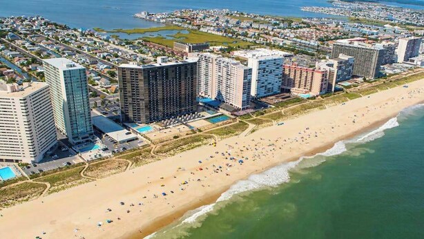 An aerial view of a coastal city with high-rise buildings, a sandy beach, and a clear view of the ocean. - Beach Club  135 D (Ocean City)