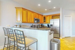 A kitchen with wooden cabinets, stainless steel appliances, a granite countertop, and a trash can. - South Beach 703 (Ocean City)