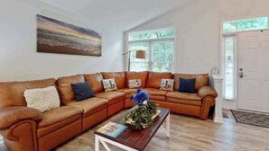 A living room with a sectional sofa, a coffee table, a painting, and a door. - Coral Shells (Ocean Pines)