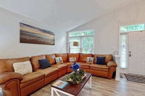 A living room with a sectional sofa, a coffee table, a painting, and a door. - Coral Shells (Ocean Pines)