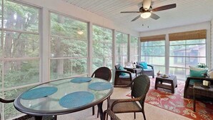 A sunroom with large windows, a ceiling fan, wicker furniture, and a glass table. - Coral Shells (Ocean Pines)