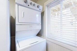 A stacked washer and dryer unit in a room with a window with blinds. - Well-Located Condo 2 Blocks from the Beach w/ AC & Private Laundry (Ocean City)