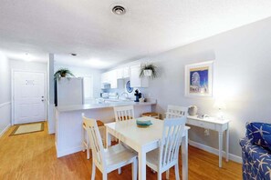 A compact kitchen with white cabinetry, a dining table with chairs, a small island with a sink, and a blue sofa in the living area. - Well-Located Condo 2 Blocks from the Beach w/ AC & Private Laundry (Ocean City)