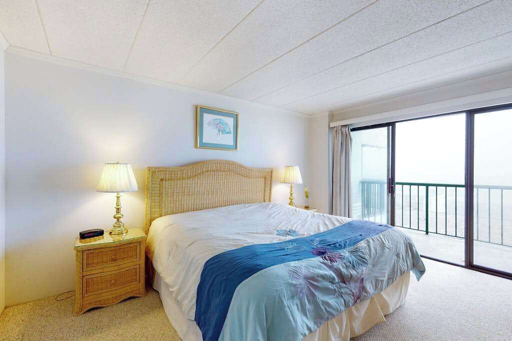 Quarto de hotel com cama, duas luminárias de cabeceira, um quadro na parede e uma varanda com vista.