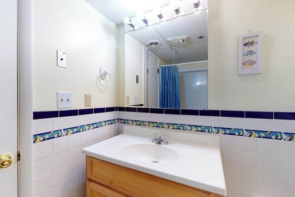 A bathroom with a white sink, a mirror, and a blue shower curtain. - Ocean View Condo with Balcony, WiFi, W/D, Central AC & Shared Outdoor Pool (Ocean City)
