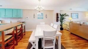 Ein Essbereich mit weißem Tisch und Stühlen, eine Küche mit türkisfarbenen Schränken und ein Wohnzimmer mit Sofa und Lampe.
