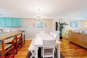 Un coin repas avec une table et des chaises blanches, une cuisine avec des meubles de couleur turquoise et un salon avec un canapé et une lampe.