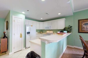 A kitchen with white cabinets, a refrigerator, a microwave, and a small island with a sink. - Bayside condo in Midtown with balcony, pool, sauna, gym & pier (Ocean City)