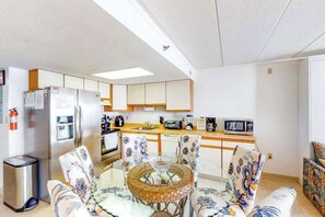 A compact kitchen with a refrigerator, microwave, and stove. There is a dining table with chairs, and a trash bin is visible. - Air-Conditioned, Oceanfront Condo with Balcony, WiFi, W/D & Shared Pool (Ocean City)