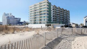 Un hotel a più piani con balconi, situato vicino a una spiaggia sabbiosa con una recinzione in legno.