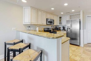 A kitchen with white cabinets, a granite countertop, a stainless steel refrigerator, and a microwave. - Updated condo in oceanfront building with side ocean view, pool, & gym (Ocean City)