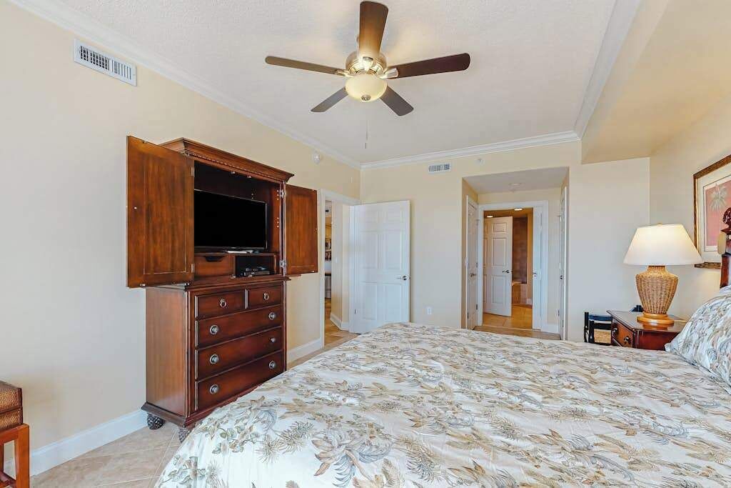 Ein Schlafzimmer mit Bett, Deckenventilator, Holzkommode und Fernseher.