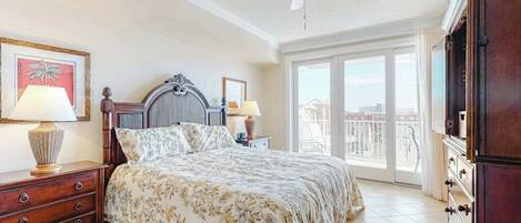 A bedroom with a bed, two bedside tables, a ceiling fan, and a view through a large window.