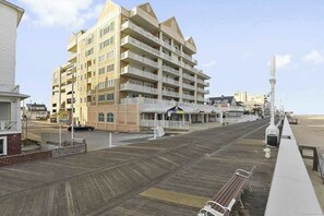 A multi-story building with balconies, a boardwalk, and a beach in the background. - Updated condo in oceanfront building with side ocean view, pool, & gym (Ocean City)
