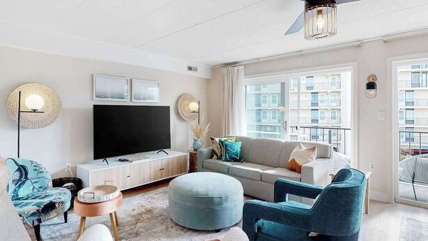 A modern living room with a flat-screen TV, a sofa, ottoman, and chairs. - Freshly Renovated Ocean Block Condo w/ Balcony, Partial Ocean View, AC & WiFi (Ocean City)
