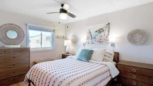 A bedroom with a bed, wooden dresser, ceiling fan, wall art, and a window. - Freshly Renovated Ocean Block Condo w/ Balcony, Partial Ocean View, AC & WiFi (Ocean City)