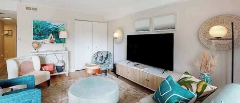 A modern living room with a flat-screen TV, a sofa, a round ottoman, and a coffee table.