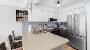 A modern kitchen with a central island, stainless steel appliances, and a microwave above the stove. - Freshly Renovated Ocean Block Condo w/ Balcony, Partial Ocean View, AC & WiFi (Ocean City)