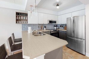 A modern kitchen with a central island, stainless steel appliances, and a microwave above the stove. - Freshly Renovated Ocean Block Condo w/ Balcony, Partial Ocean View, AC & WiFi (Ocean City)