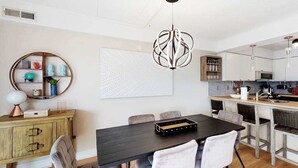 A modern kitchen with white cabinets, a black dining table, and a unique pendant light. - Freshly Renovated Ocean Block Condo w/ Balcony, Partial Ocean View, AC & WiFi (Ocean City)
