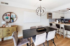 A modern kitchen with white cabinets, a black dining table, and a unique pendant light. - Freshly Renovated Ocean Block Condo w/ Balcony, Partial Ocean View, AC & WiFi (Ocean City)