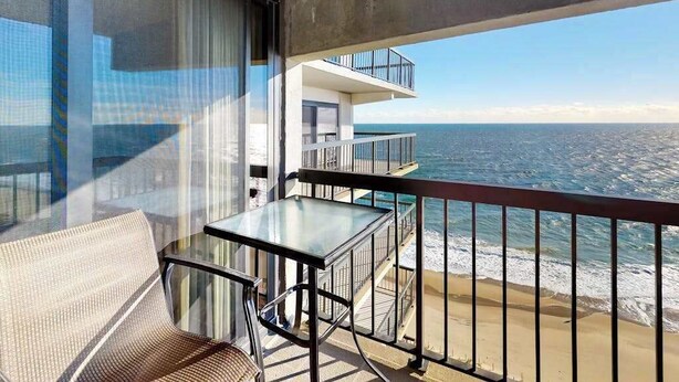 En balkon med et glasbord og en stol, havudsigt og en bygning med balkoner.