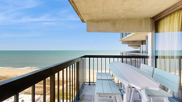 Ein Balkon mit Blick auf Strand und Meer, ein Tisch und eine Bank.