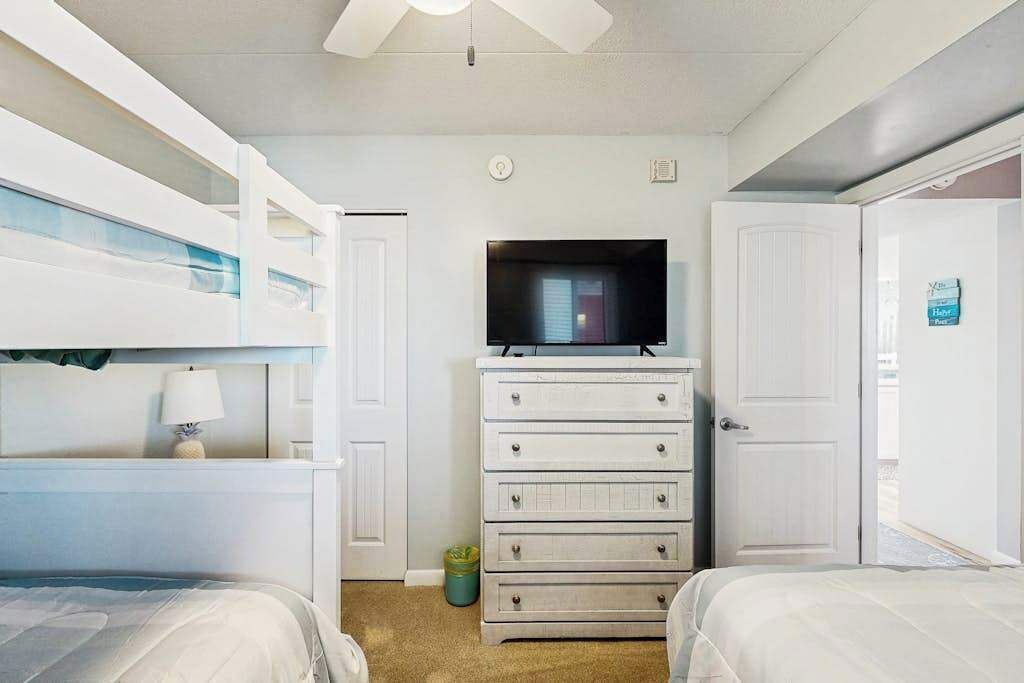 Une chambre d’hôtel avec des lits superposés, un téléviseur posé sur une commode et une porte avec une pancarte.