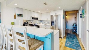 Una cocina moderna con armarios blancos, una isla central, electrodomésticos de acero inoxidable y un tapete azul estampado.