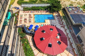 A rooftop pool area with lounge chairs, a swimming pool, and a large red umbrella. - Convenient & budget-friendly beach condo with balcony, pools, sauna & gym (Ocean City)