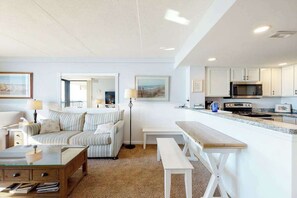 A modern living room with a sofa, a coffee table, and a dining area with a bench. - Incredible & well-equipped beach condo with pools, gym, sauna & game room (Ocean City)
