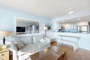 A living room with a sofa, coffee table, and a view into the kitchen area. - Incredible & well-equipped beach condo with pools, gym, sauna & game room (Ocean City)