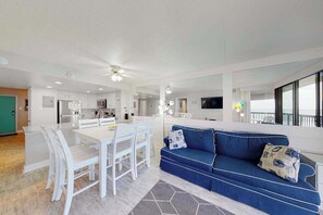 A modern living space with a dining area, a sofa, and a kitchen. - Unbeatable beach condo with balcony, W/D, pools, game room & gym (Ocean City)