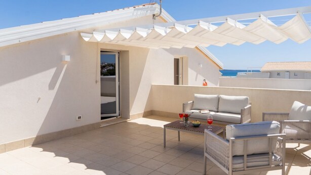 Una terraza en la azotea con un sofá blanco para exteriores, una mesa pequeña con un cuenco y una copa, y vistas al mar.