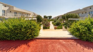 Un sendero conduce a una hilera de edificios modernos con balcones, rodeado de vegetación y cactus.
