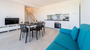 Una cocina moderna con armarios blancos, una zona de comedor con una mesa y sillas, un sofá azul y un televisor.