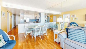 A modern living room with a dining area, kitchen, and a large mirror reflecting the space. - Updated, ocean-view condo with balcony, pools, saunas, game room & gym (Ocean City)