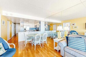 A modern living room with a dining area, kitchen, and a large mirror reflecting the space. - Updated, ocean-view condo with balcony, pools, saunas, game room & gym (Ocean City)