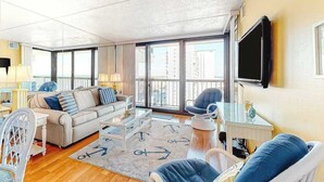 A living room with a sofa, armchairs, a coffee table, and a TV. - Updated, ocean-view condo with balcony, pools, saunas, game room & gym (Ocean City)