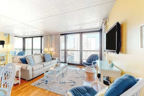 A living room with a sofa, armchairs, a coffee table, and a TV. - Updated, ocean-view condo with balcony, pools, saunas, game room & gym (Ocean City)