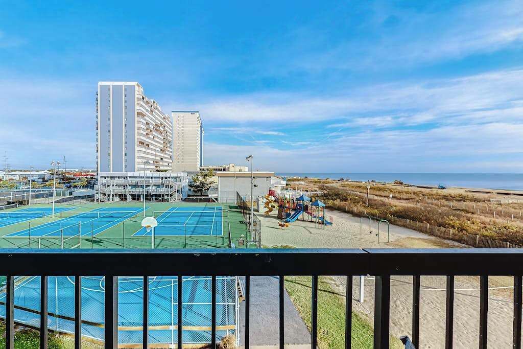 Vista di un campo sportivo con un'area giochi, un edificio alto e una spiaggia sullo sfondo.
