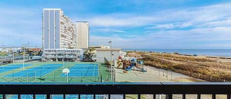 Vista di un campo sportivo con un'area giochi, un edificio alto e una spiaggia sullo sfondo.