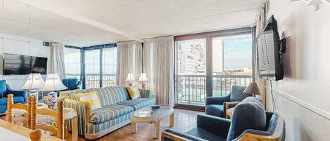 Et moderne hotelværelse med opholdsområde, der indeholder en sofa, lænestole, et sofabord og et fjernsyn.