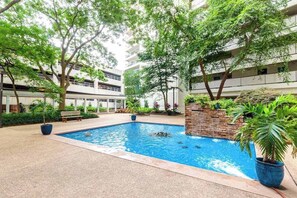 Una piscina rodeada de vegetación y un edificio de varios pisos al fondo.