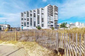 A high-rise building with multiple balconies, a sandy foreground, and a clear sky. - Sea Terrace 1401 (Ocean City)