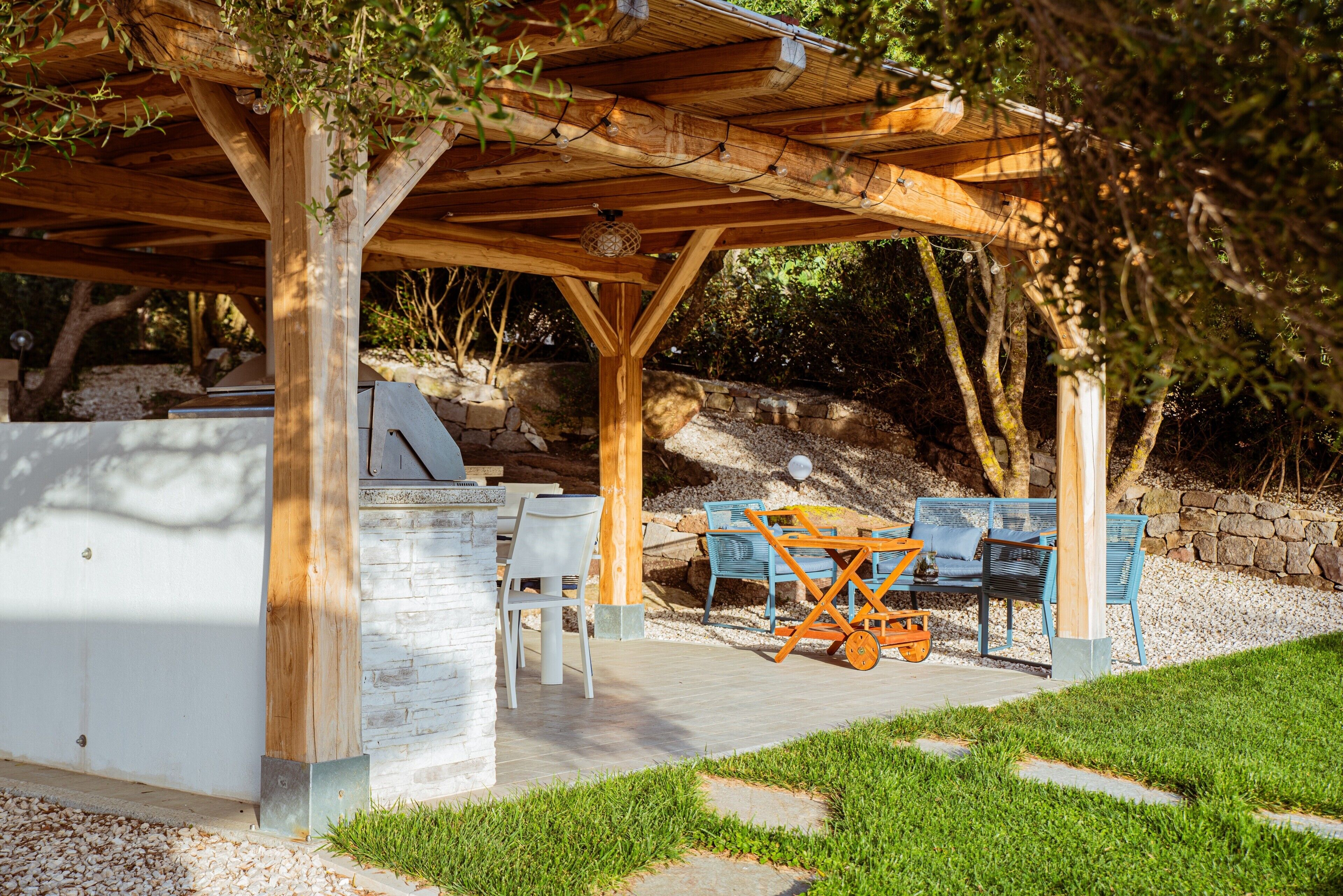 An outdoor patio with a wooden pergola, stone seating, and a barbecue grill.