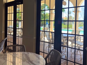 Ein Zimmer mit einem Marmortisch und Korbstühlen, große Fenster mit Blick auf Gartenmöbel und einen Pool.