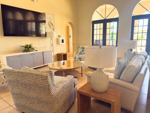 Ein Wohnzimmer mit Sofa, Sessel, Couchtisch und einem an der Wand montierten Fernseher.