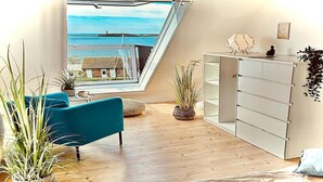Een kamer met uitzicht op zee, een blauwe bank, een witte dressoir en verschillende potplanten.